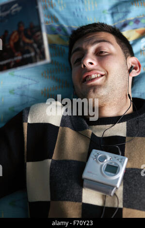 Jeune homme couché sur le lit de l'écoute d'un minidisc ; modèle libéré pour une utilisation dans la lutte contre le VIH et le sida, Banque D'Images