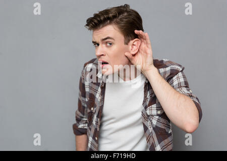 Les jeunes curieux beau mâle en chemise à carreaux essayant d'écouter les rumeurs Banque D'Images
