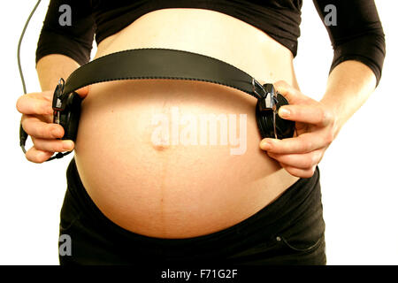 Les bras sur le ventre du ventre de maman enceinte holding écouteurs pour aimer la musique bébé fond blanc Banque D'Images