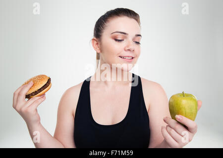 Portrait of a happy grosse femme choisir entre burger ou apple isolé sur fond blanc Banque D'Images