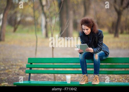 Portrait d'une femme assis sur le banc et using tablet computer in autumn park Banque D'Images