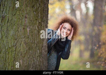 Portrait d'une femme souriante avec des cheveux bouclés, à l'arrière un arbre en automne park Banque D'Images