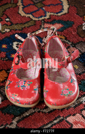 Une paire bien usé de la petite fille chaussures en cuir rouge vif placé sur un tapis. Banque D'Images