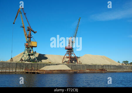 Sable de chargement avec l'aide d'une grue sur une péniche sur l'eau et le fond de ciel de sable jaune. Banque D'Images