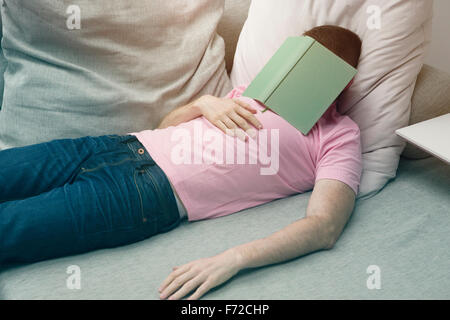 L'homme en jeans et tshirt dormir sur table avec le livre sur la tête Banque D'Images