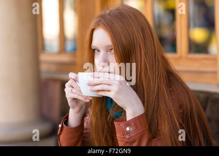 Réfléchis attrayant fille mignonne avec de beaux cheveux long rouge de boire du café en terrasse d'un café Banque D'Images