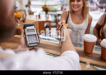 Le client paie pour sa commande avec une carte de crédit dans un café. Bartender holding un lecteur de carte de crédit et le retour de la machine la d Banque D'Images