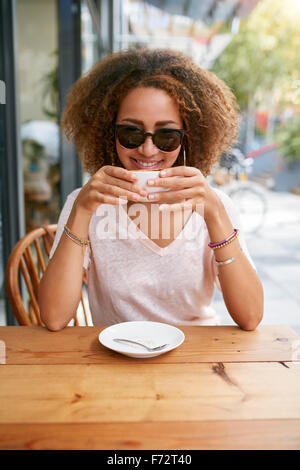 Portrait of young African woman drinking coffee at sidewalk cafe. Charmante fille avec des cheveux bouclés tenant une tasse de café, Banque D'Images