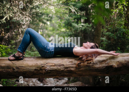 Femme allongée sur le dos sur un tronc d'arbre tombé dans une forêt. Banque D'Images