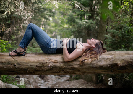 Femme allongée sur le dos sur un arbre dans une forêt. Banque D'Images