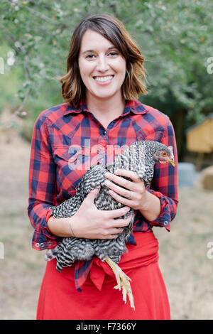 Portrait of a smiling woman holding a gray specked hen. Banque D'Images