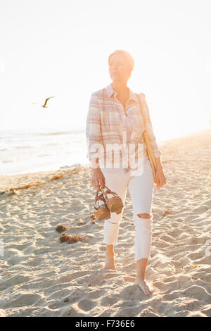 Femme marchant le long d'une plage de sable fin à l'océan. Banque D'Images