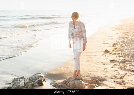 Femme marchant le long d'une plage de sable fin à l'océan. Banque D'Images