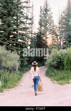 Femme marchant le long d'un chemin forestier, portant un sac. Banque D'Images