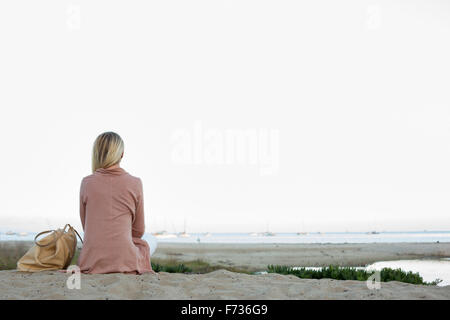 Femme blonde assise sur une plage de sable. Banque D'Images