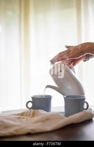 On verse de l'eau chaude à partir d'un pot de café dans un mug. Banque D'Images