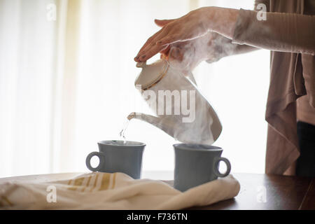 Close up of a woman pouring l'eau chaude à partir d'un pot de café dans un mug. Banque D'Images