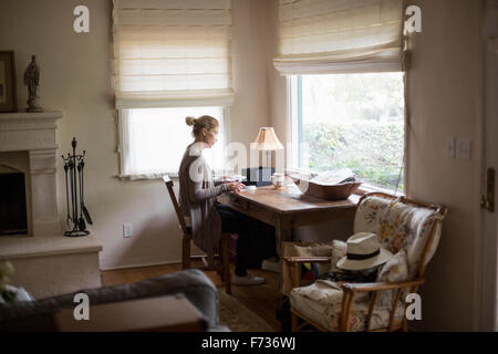 Femme blonde assis à un bureau par une fenêtre, en regardant des photos. Banque D'Images