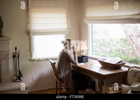 Femme blonde assis à un bureau par une fenêtre, de boire une tasse de thé. Banque D'Images