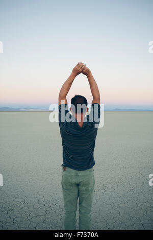 L'homme s'étend avec les bras au-dessus de la tête, faisant face à l'aube sur vaste désert, Black Rock Desert, Nevada Banque D'Images