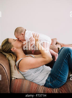 Une femme allongée sur un canapé à jouer avec une petite fille, l'embrassant la joue.