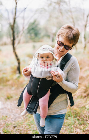 Une femme portant des lunettes portant un bébé portant un chapeau blanc dans un porte-bébé avant. Banque D'Images