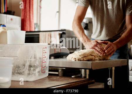 Un homme, un boulanger travaillant dans une cuisine commerciale le pétrissage un grand morceau de pâte. Banque D'Images