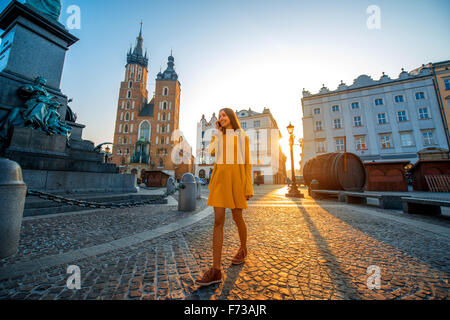 Jeune et belle femme en robe jaune, marchant et parlant avec un téléphone mobile dans le vieux centre-ville de Cracovie le matin Banque D'Images