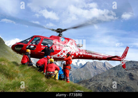 Les secouristes sont à la montagne avec l'atterrissage d'un hélicoptère d'Air Zermatt sur une pente herbeuse dans les Alpes suisses. Banque D'Images