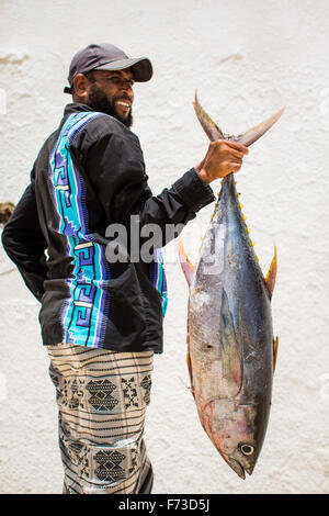 LAMU, Kenya, Afrique. Un homme en costume traditionnel est titulaire d'un lage rouge par la queue contre un mur en stuc blanc. Banque D'Images