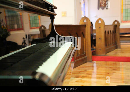 Close-up d'un piano à queue noir dans une église, avec des bancs d'église en arrière-plan Banque D'Images