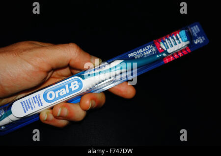 Une main tenant une brosse à dents Oral B dans son emballage' photographié sur un fond noir. Banque D'Images