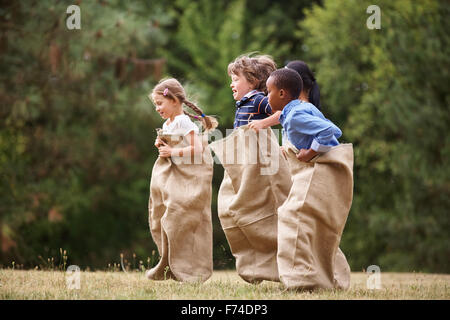 L'Interracial groupe d'enfants qui participent à une course de sac en été Banque D'Images