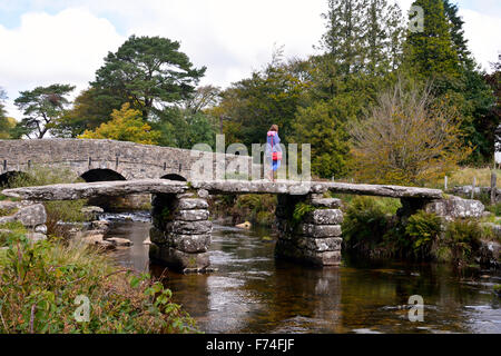 Woman Crossing sur la clapper bridge à Postbridge à Dartmoor, dans le Devon, Angleterre Banque D'Images