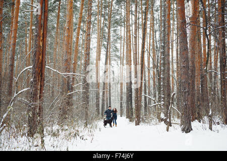 Jeune couple avec un chien s'amusant dans la forêt d'hiver les jours fériés. Vue générale. L'espace de copie pour le texte. Banque D'Images