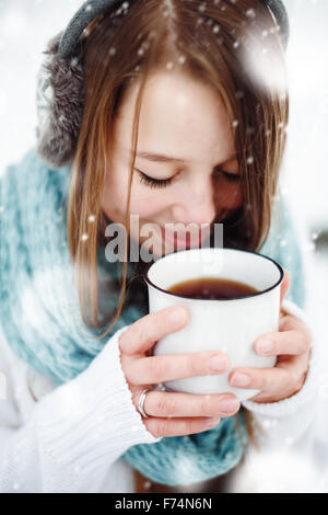 Belle jeune femme de boire une boisson chaude à l'extérieur en hiver. Close Up Portrait. Tirée de la neige. Focus sélectif. Banque D'Images