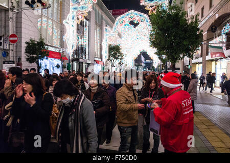 Le Japon, Kobe. Des foules de gens marcher dans la rue festival lumière luminaire annuelle tandis que le personnel d'affichage dans des tenues de Noël collecte de dons. Banque D'Images