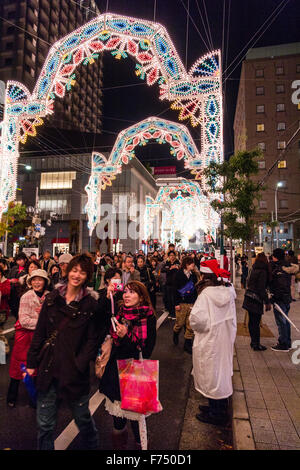 Le Japon, Kobe. Des foules de gens marcher dans la rue festival lumière luminaire annuelle tandis que le personnel d'affichage dans des tenues de Noël collecte de dons. Banque D'Images