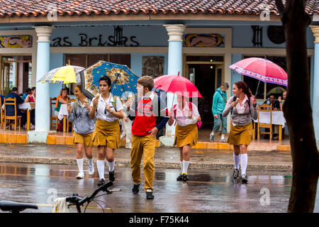 Les écoliers, les étudiants à traverser une rue, pluie de Vinales, parapluies, manger de la crème glacée, Viñales, Cuba, Pinar del Rio, Cuba, Street Banque D'Images