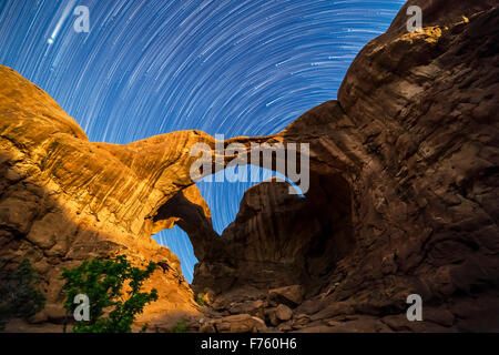 Étoiles circumpolaires spinning derrière arc double à Arches National Park, Utah, comme la Lune gibbeuse lights l'Arches Banque D'Images