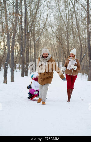 Happy man pulling sled avec des enfants dans winter park Banque D'Images