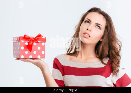 Portrait d'une jeune pensive woman holding gift box isolé sur fond blanc Banque D'Images