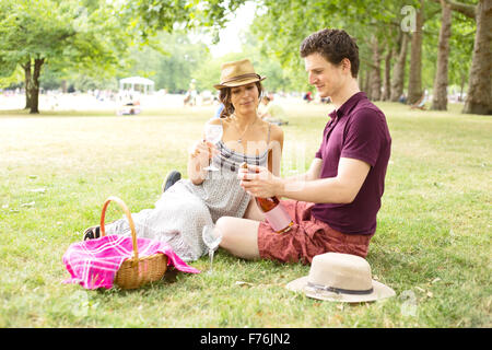 Jeune couple assis dans le parc ayant un pique-nique Banque D'Images