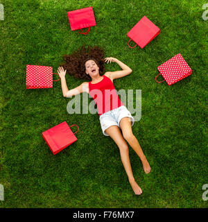 Belle et heureuse jeune femme couché dans l'herbe entouré par des sacs-cadeaux rouge Banque D'Images