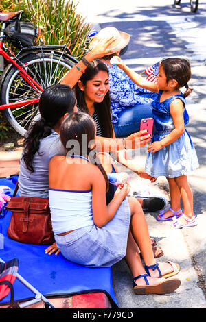 Famille de quatre sœurs Hispaniques s'asseoir sur le trottoir en tenant vos autoportraits en attendant la parade du 4 juillet à Santa Barbara Banque D'Images