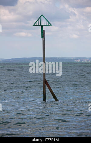 Un panneau d'avertissement fait d'un morceau de l'ancienne voie de chemin de fer avec un triangle vert sur le poste en mer au large de la plage. Banque D'Images