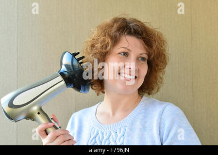 Femme boucles avec un sèche-cheveux avec diffuseur Banque D'Images