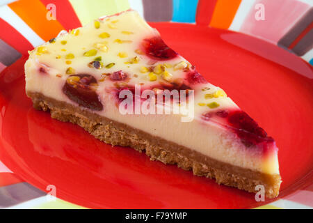 Tesco finest & Framboise cheesecake Pistache tranche sur la plaque de couleur rouge Banque D'Images