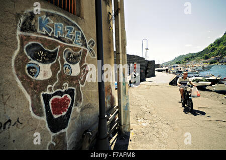 Jeune homme monté sur un cyclomoteur et graffiti à Santa Maria la Scala, Acireale, Sicile, Italie Banque D'Images