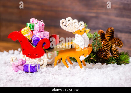 Composition de Noël Décoration renne et Santa sleigh avec cadeaux, sapin, de la direction générale de cocottes dans la neige sur le sol en bois backgroun Banque D'Images